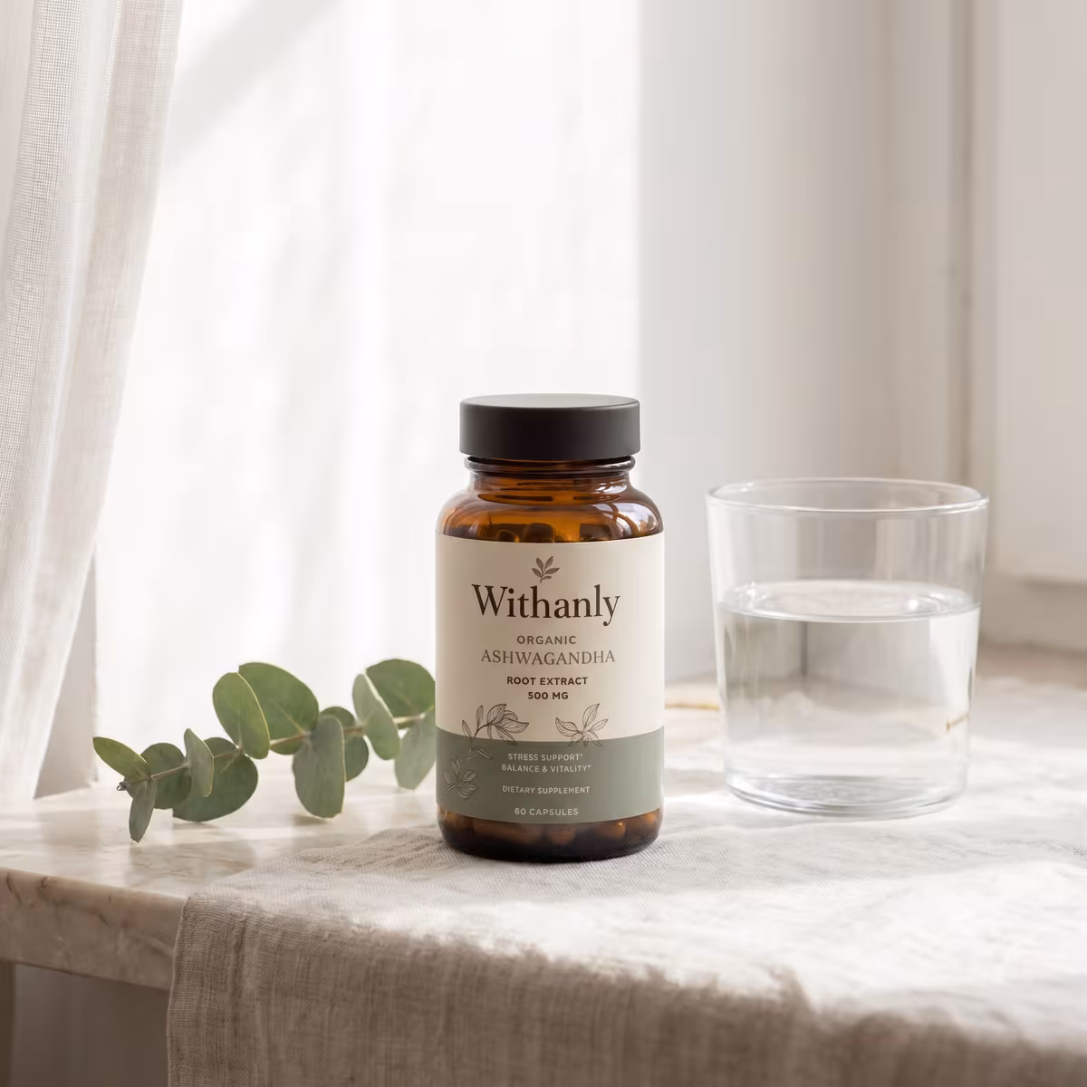 The Withanly ashwagandha bottle on a warm oak table in early-evening light, beside two ceramic mugs of tea and a child's crayon drawing, with a softly lit living room behind — a calm, present home