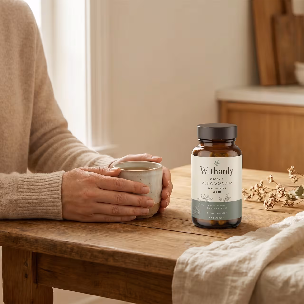 A person's hands calmly cradling a warm ceramic mug at a sunlit wooden table, with the Withanly ashwagandha bottle resting beside it